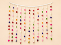 Blooming Welcome Handcrafted Crochet Floral Toran – rainbow mini flowers cascading from white header bar with miniature crochet figures at tips