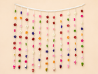 Blooming Welcome Handcrafted Crochet Floral Toran – rainbow mini flowers cascading from white header bar with miniature crochet figures at tips