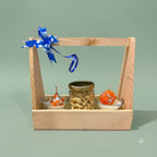 Diwali Gift Hamper with Fragrance showing two scented mithai candle bowls, a dry-fruit jar, wooden holder, and greeting card